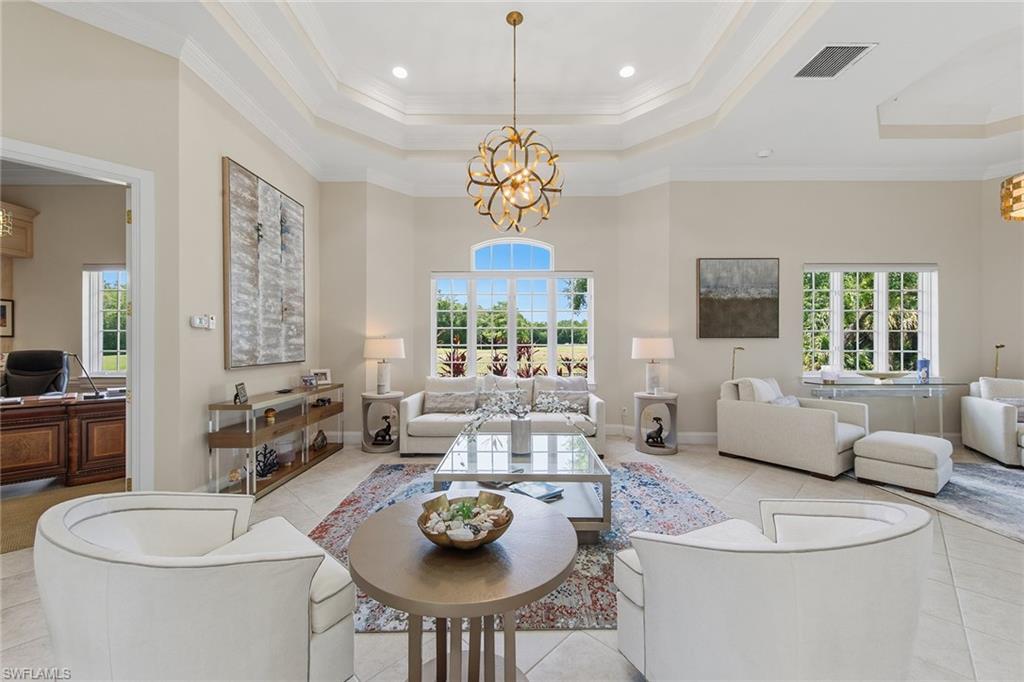 Furnished living room with white sofas, a sculptural gold chandelier, and large windows overlooking greenery.