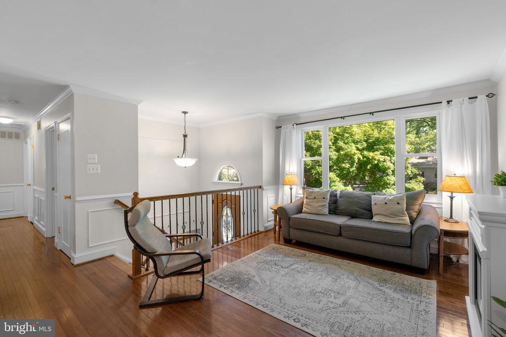 Living room with a gray sofa, hardwood floors, and large windows overlooking leafy trees.