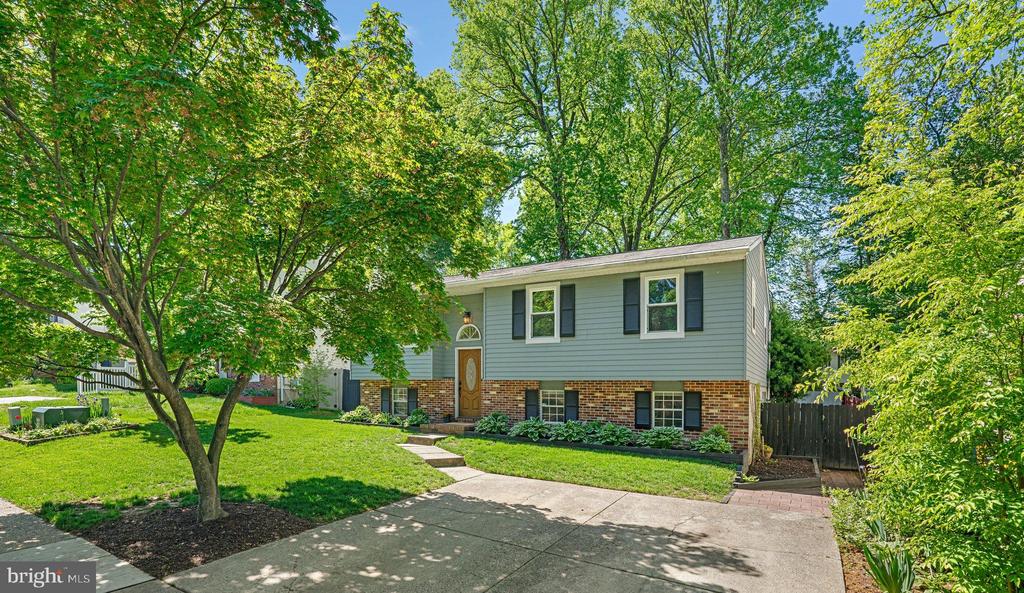 Split-level home with blue-gray siding, brick lower facade, and mature trees framing the front yard.