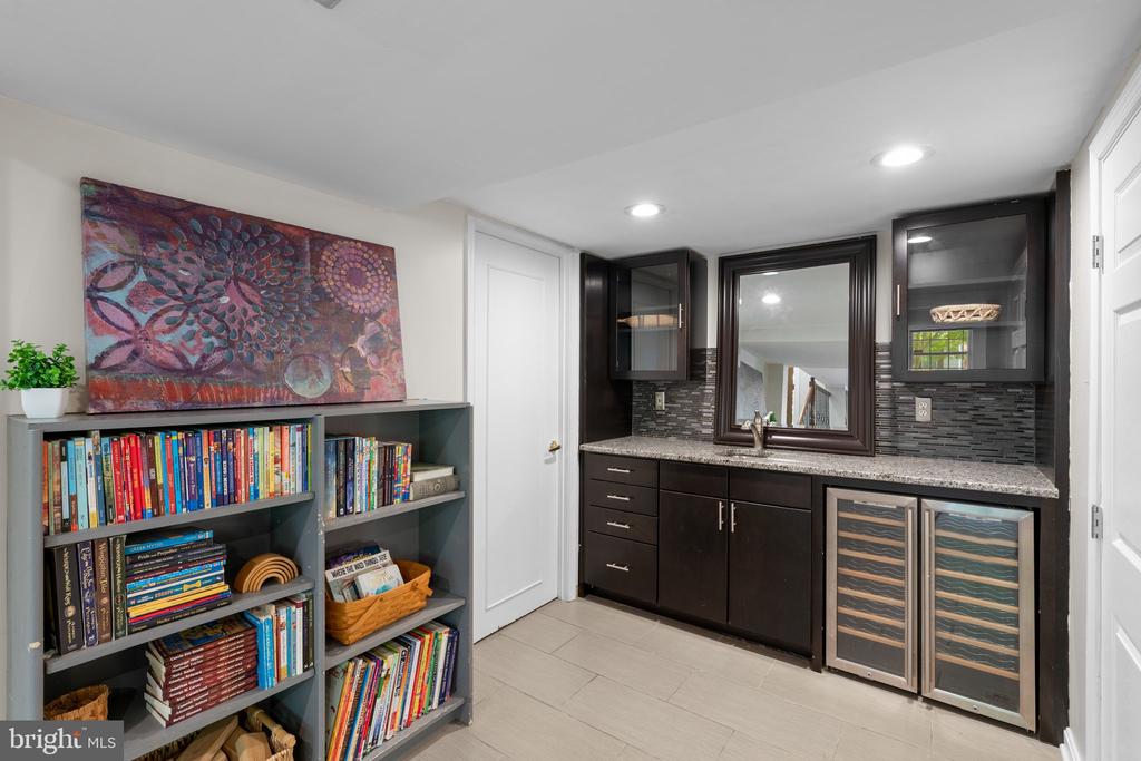 Home bar with dark cabinetry and wine refrigerators beside built-in bookshelves filled with books.