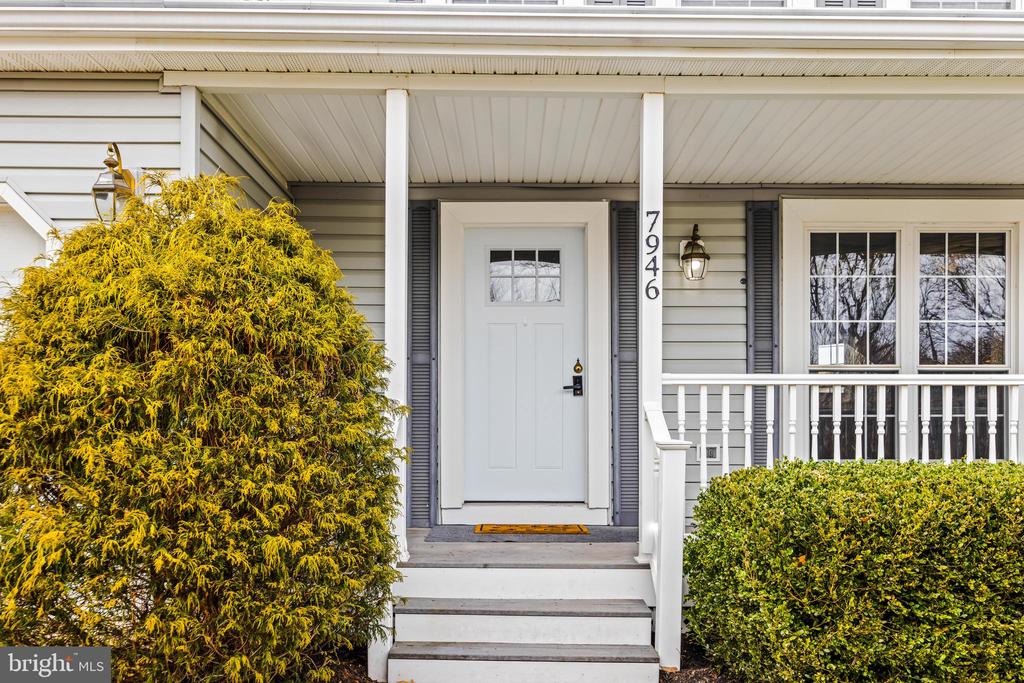 House entrance with white front door, covered porch, steps, and address 7946 beside the door.