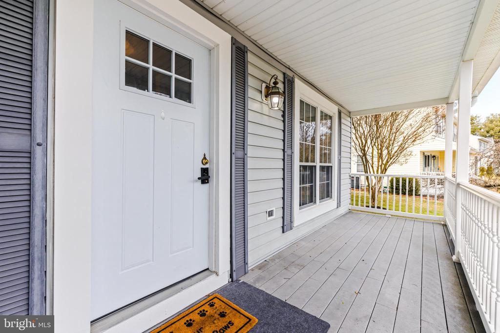 Covered front porch with a white entry door, gray siding, and white railing.