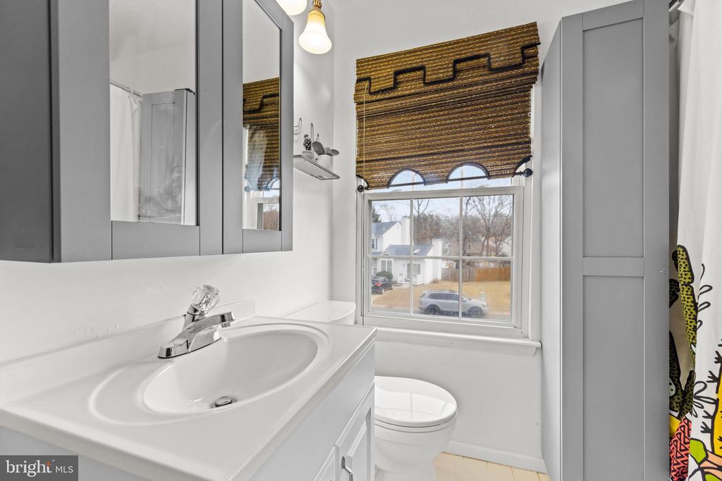 Bathroom with a white vanity, gray mirrored cabinets, and a window with a brown woven shade.