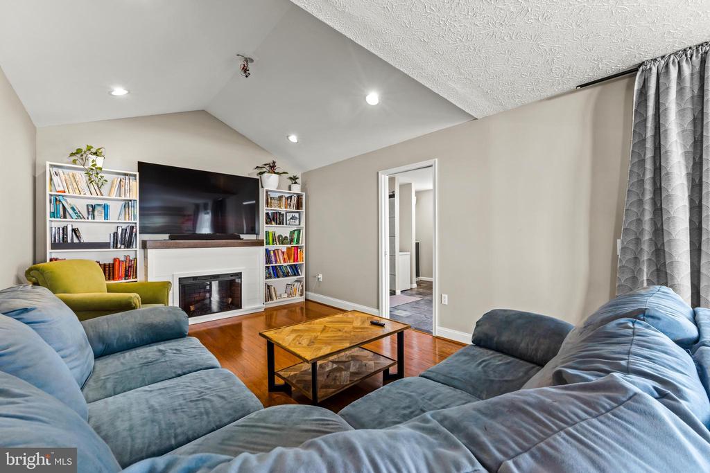 Living room with blue sectional sofas, a vaulted ceiling, and a fireplace beneath a television.