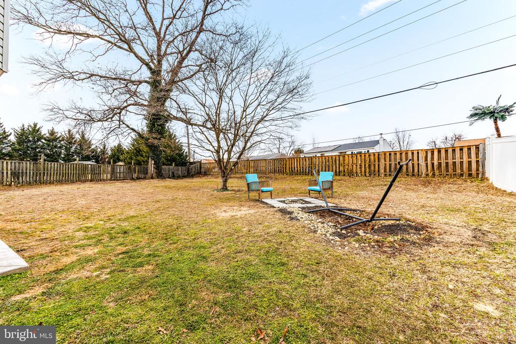 Fenced backyard with leafless trees, turquoise chairs, stepping stones, and a metal swing frame.