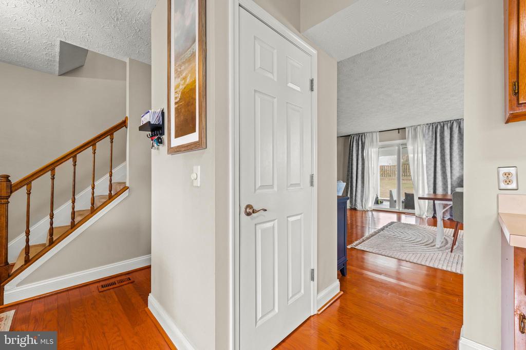 Entry hall with hardwood floors, a wooden staircase, and an open doorway to a bright living area.
