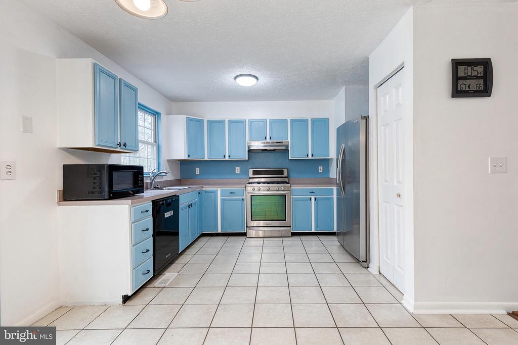Kitchen with light blue cabinets, stainless steel appliances, and white tile flooring.