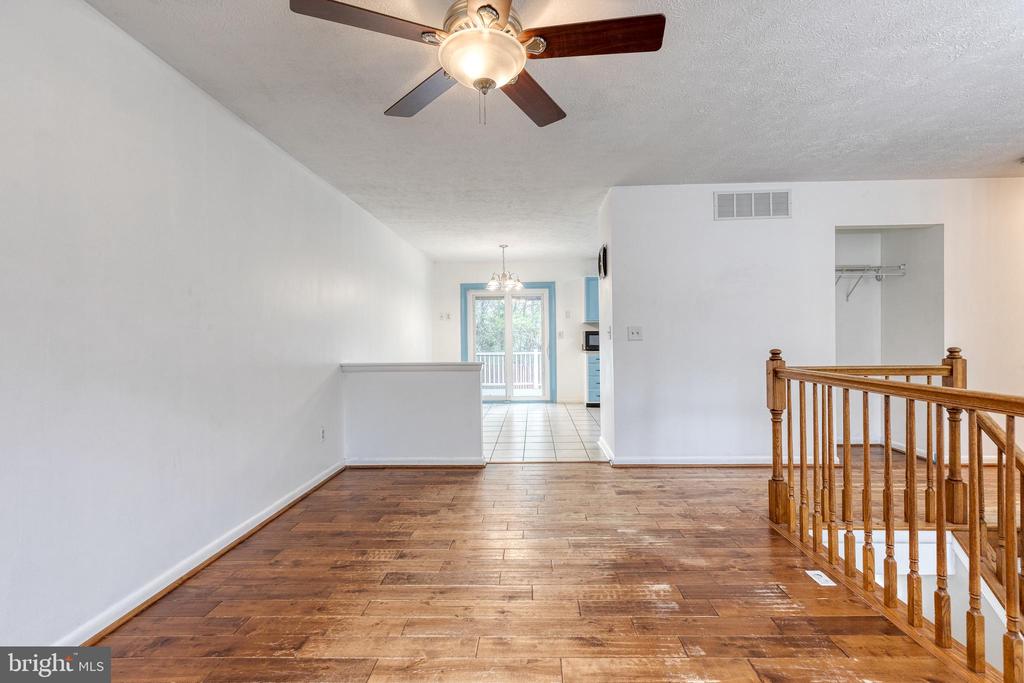 Unfurnished living area with hardwood floors, a ceiling fan, and a wooden stair railing.