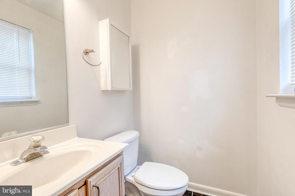 Bathroom with a white sink, wood vanity, toilet, mirrored cabinet, and windows with blinds.