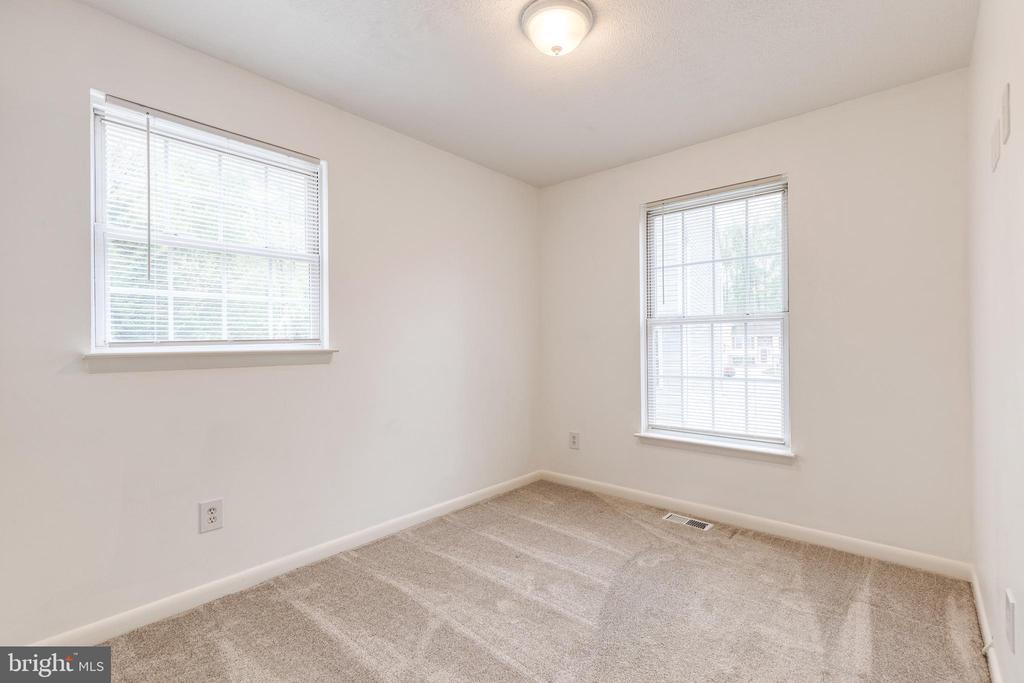 Empty bedroom with beige carpet, two windows with blinds, and a ceiling light.