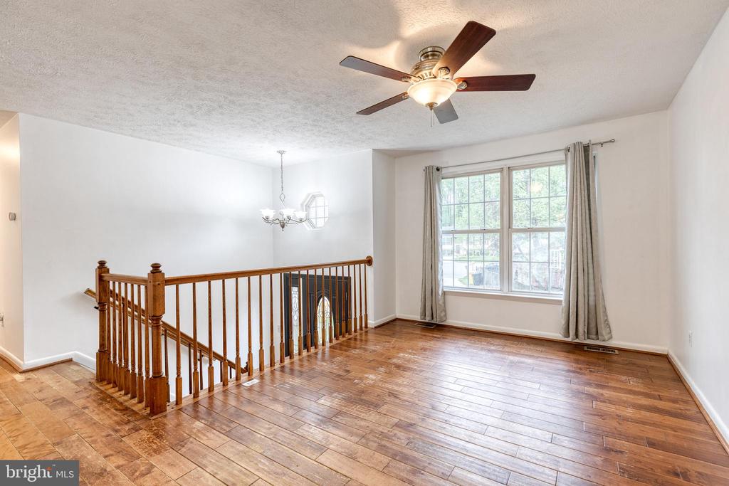Upstairs landing with hardwood floors, wooden stair railing, large curtained window, and ceiling fan.