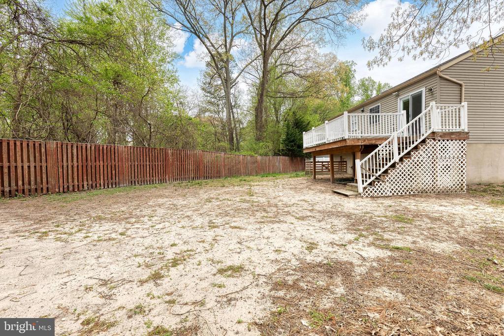 Sandy backyard with a raised deck, white stairs, wooden fence, and mature trees.