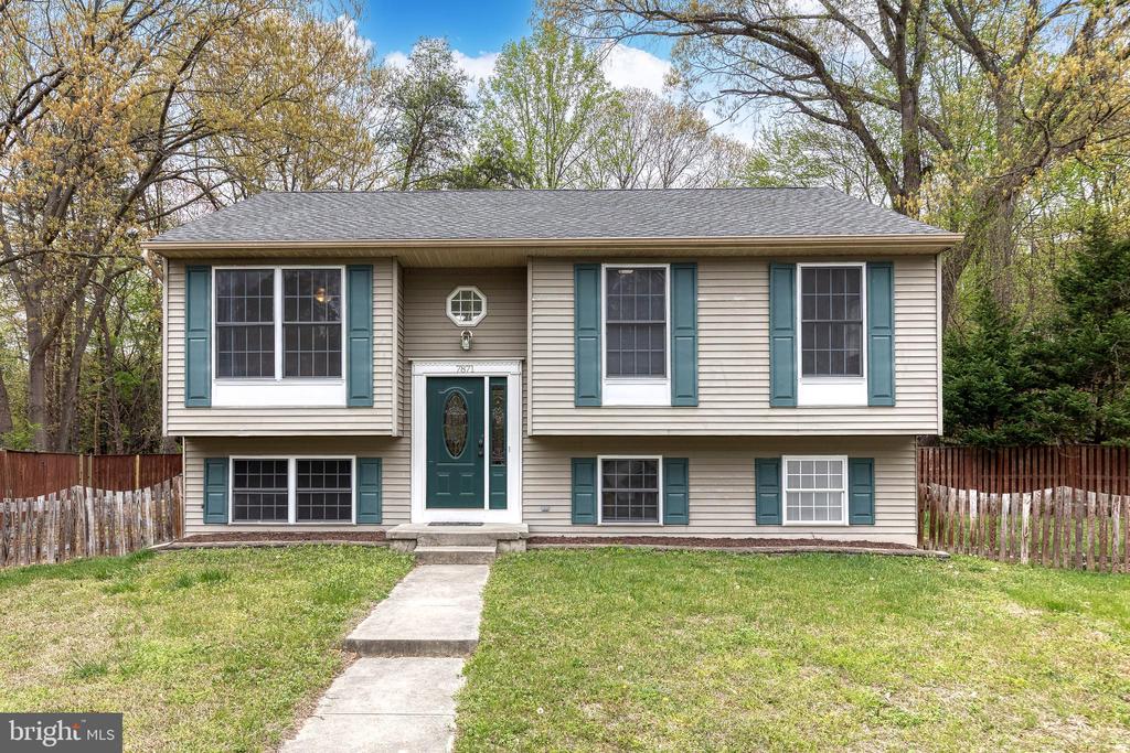 Beige split-level home with teal shutters and front door, viewed from the lawn along its concrete walkway.