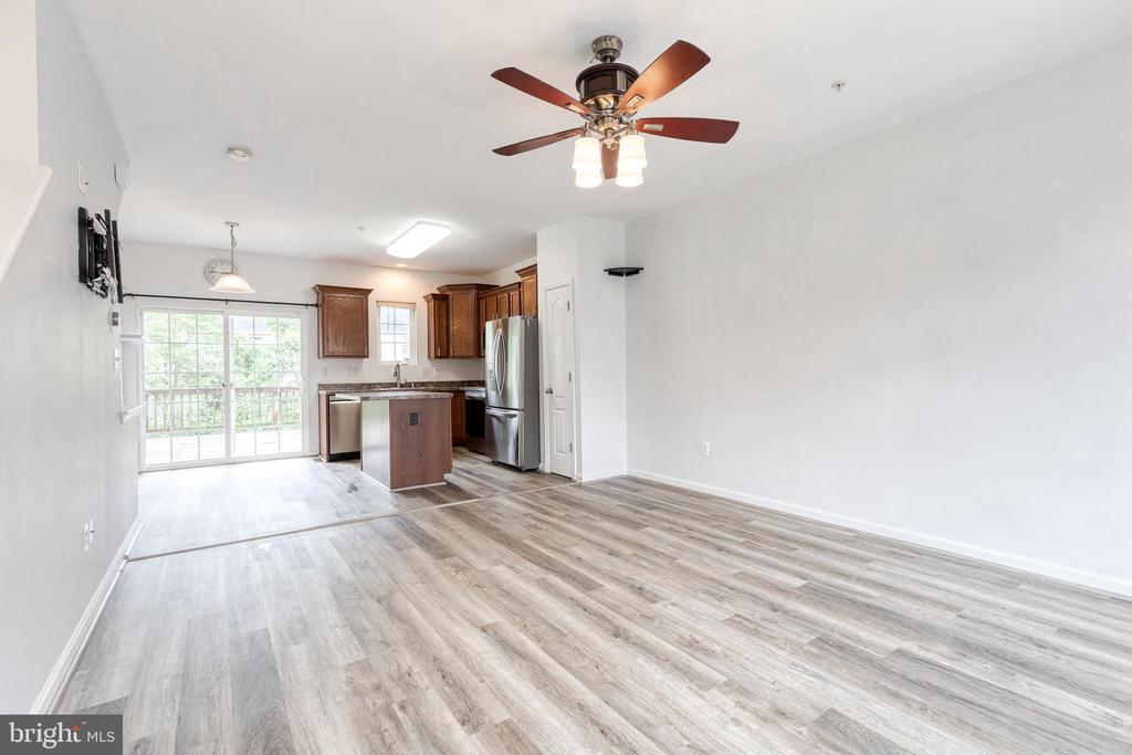 Open-plan living area with gray flooring, a ceiling fan, and a kitchen beside sliding glass doors.
