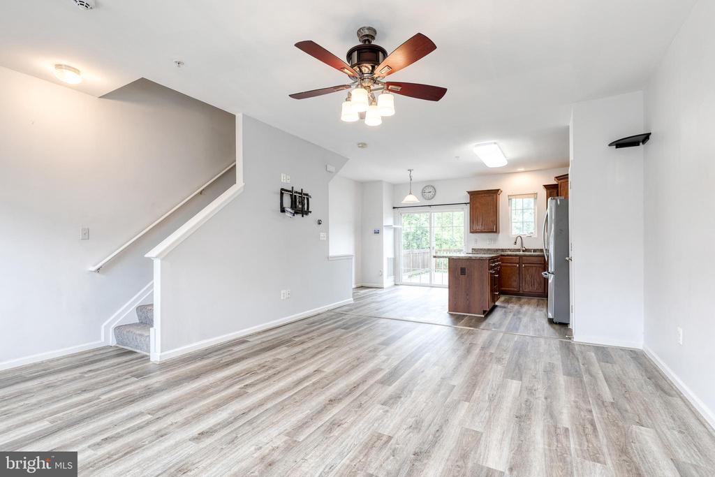 Vacant open-plan living area with gray plank flooring, staircase, and kitchen with dark wood cabinets.