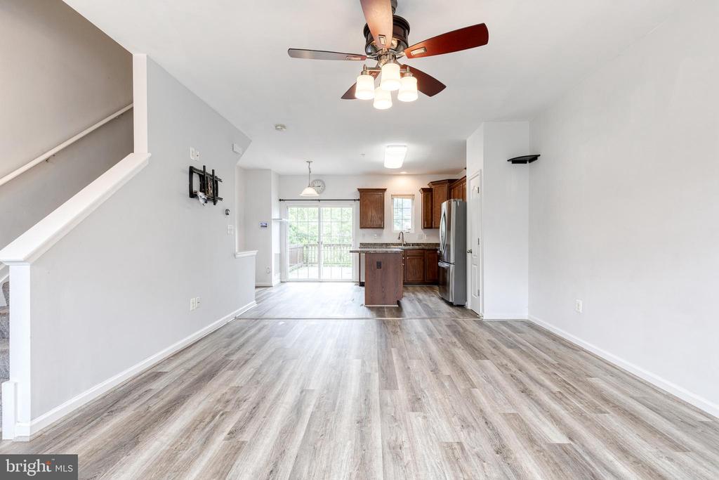 Open living area with gray wood-look flooring, a ceiling fan, and a kitchen at the far end.