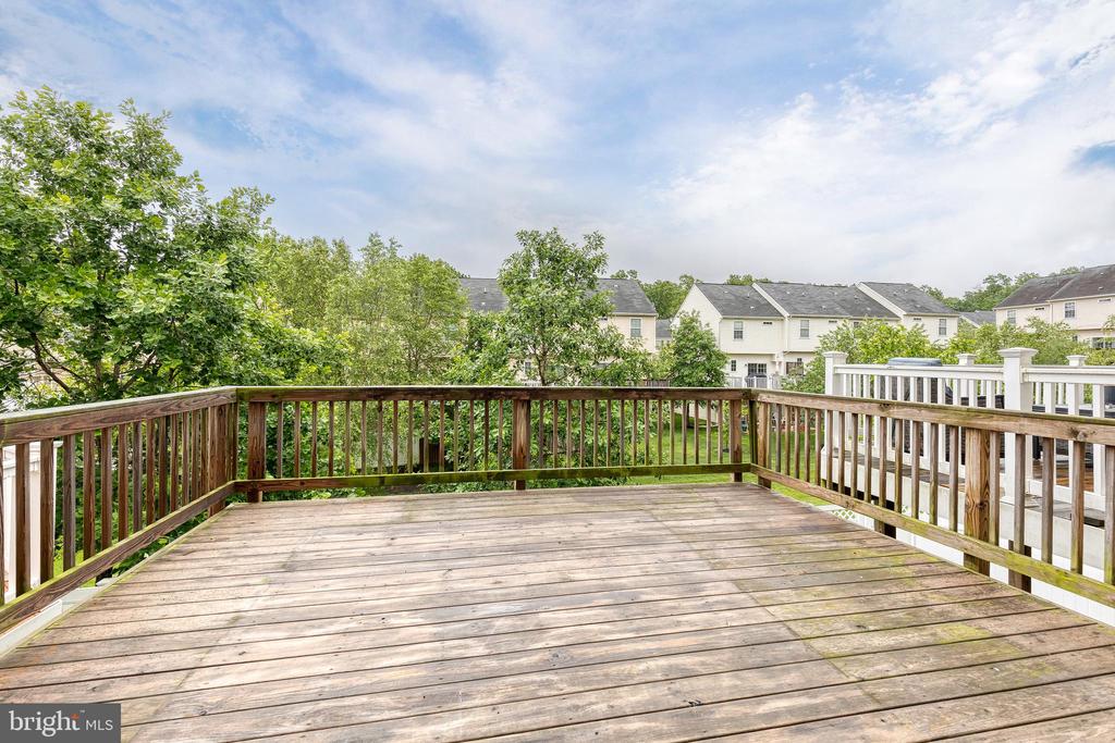 Expansive wood deck with railings overlooking trees and neighboring houses.