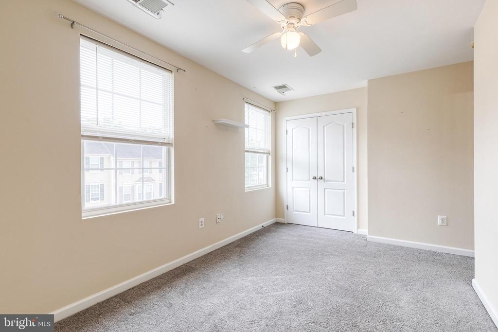 Empty carpeted bedroom with two windows, a ceiling fan, and a double-door closet.