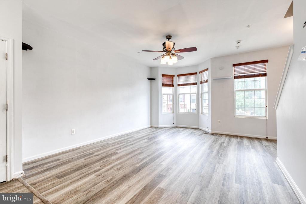 Empty living room with gray flooring, a ceiling fan, and windows with wood blinds.