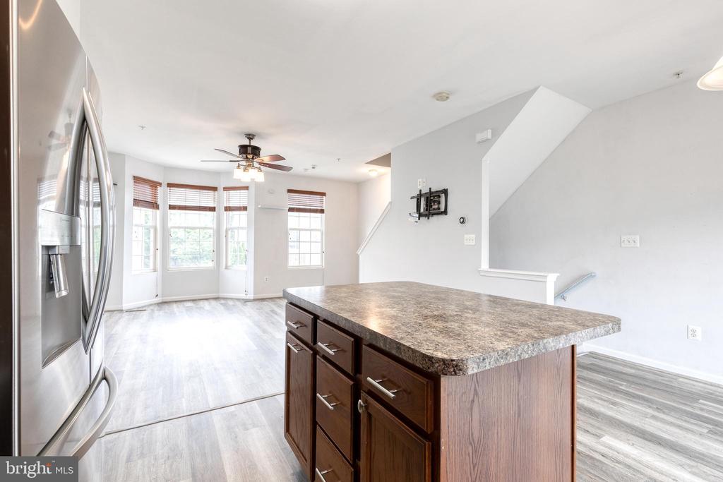 Vacant kitchen with a large dark-wood island, stainless-steel refrigerator, and bay windows in the adjoining living area.