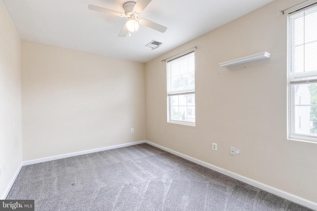 Vacant bedroom with gray carpet, two windows, and a ceiling fan with light.