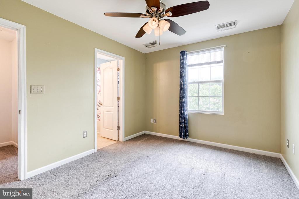 Empty bedroom with gray carpet, a ceiling fan, and a window with blue curtains.