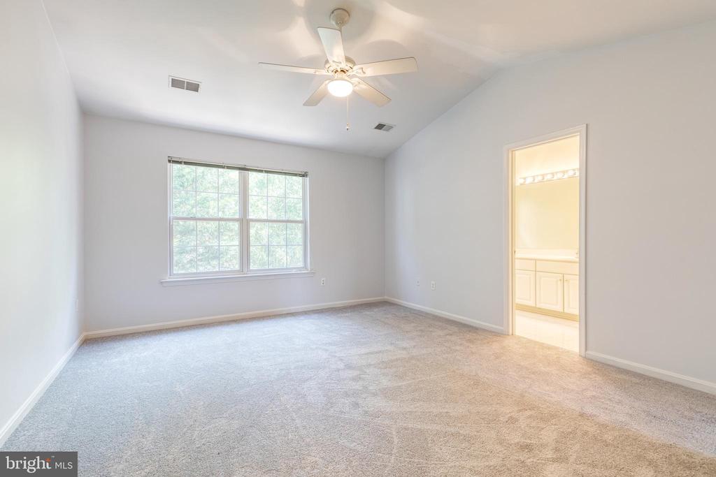 Empty carpeted bedroom with a ceiling fan, wide window, and adjoining bathroom vanity.