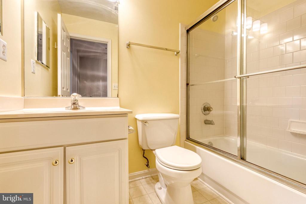 Bathroom with a white vanity, toilet, and tiled tub-shower behind glass doors.