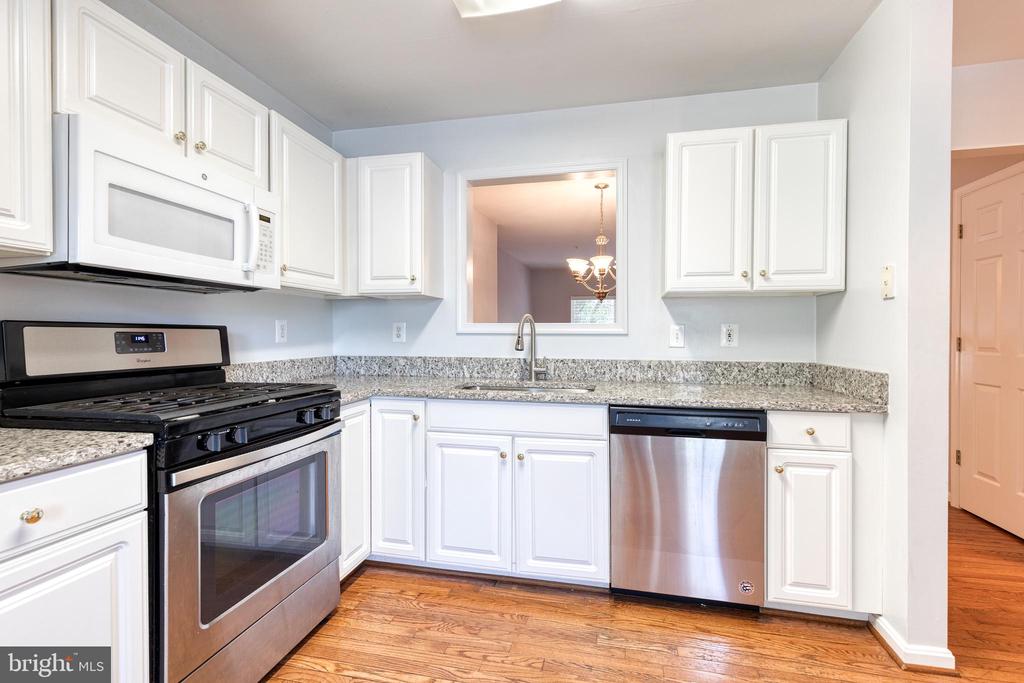 Kitchen with white cabinetry, granite counters, stainless appliances, and warm wood flooring.