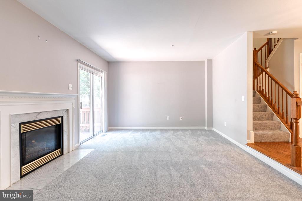 Empty living room with a marble-surround fireplace, sliding glass door, and staircase with wood railing.