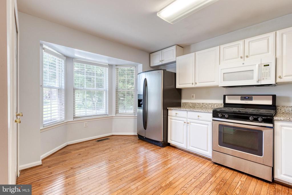 Vacant kitchen with white cabinets, stainless appliances, hardwood floors, and a bay window.
