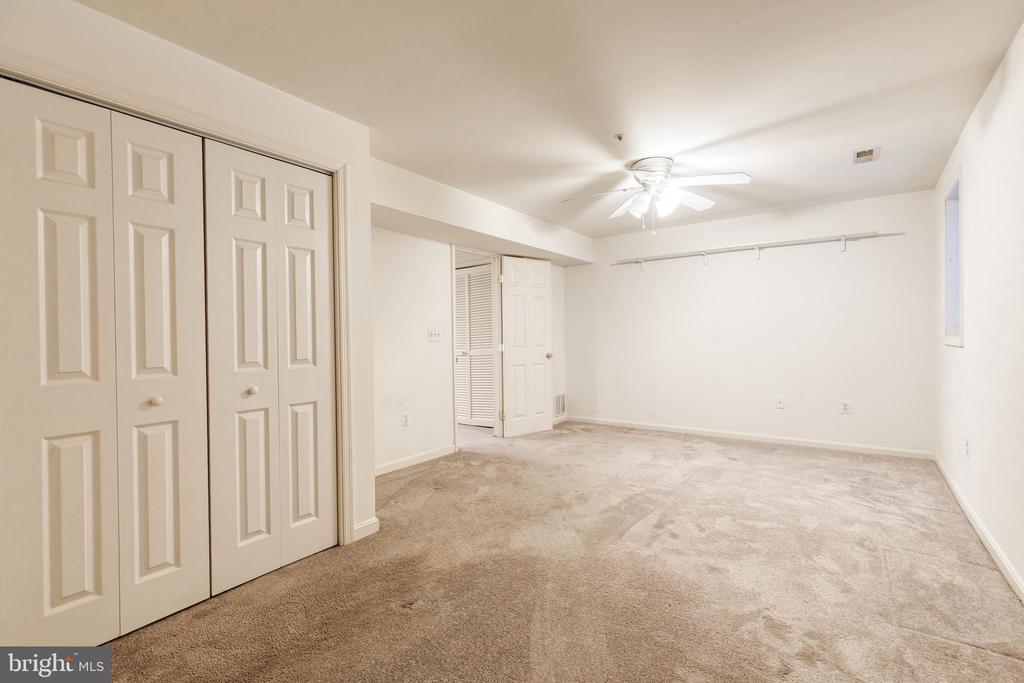 Empty carpeted bedroom with white closet doors and a ceiling fan.