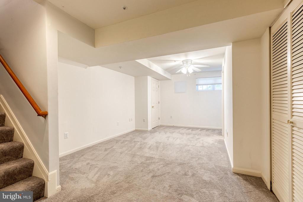 Carpeted lower-level room with a staircase, louvered closet doors, and ceiling fan.