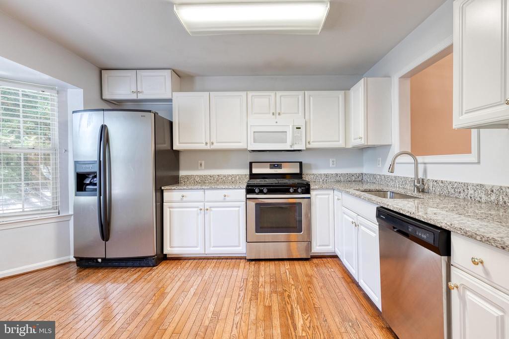 Kitchen with white cabinets, granite countertops, stainless steel appliances, and warm hardwood floors.