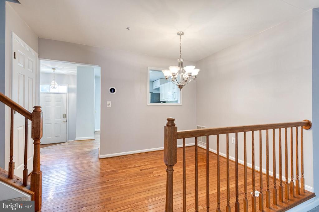 Unfurnished entry landing with polished hardwood floors, a chandelier, and wooden stair railing.
