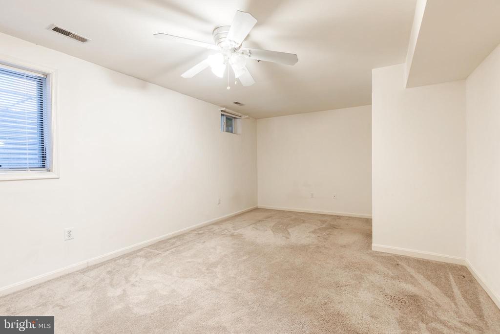 Empty carpeted room with a ceiling fan and two small windows.
