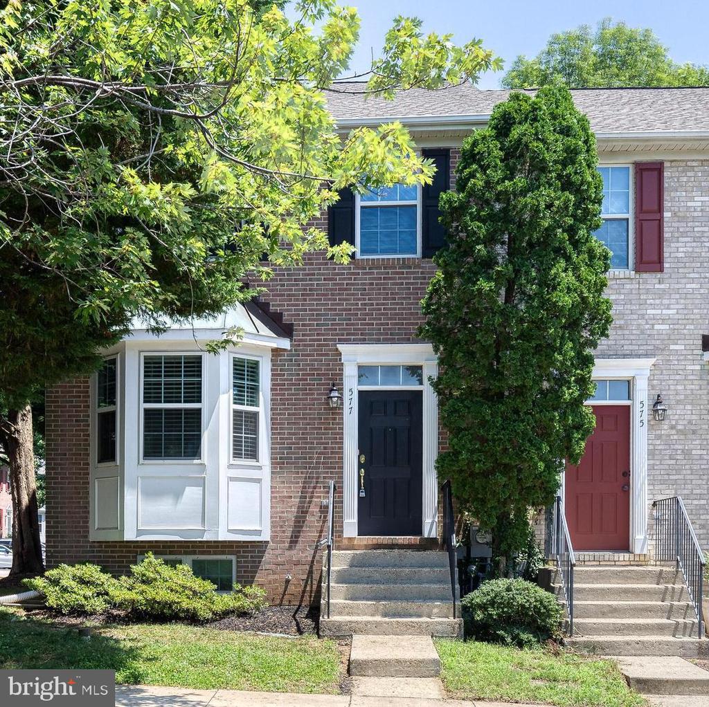 Brick townhouse with a black entry door, white bay window, and mature trees.