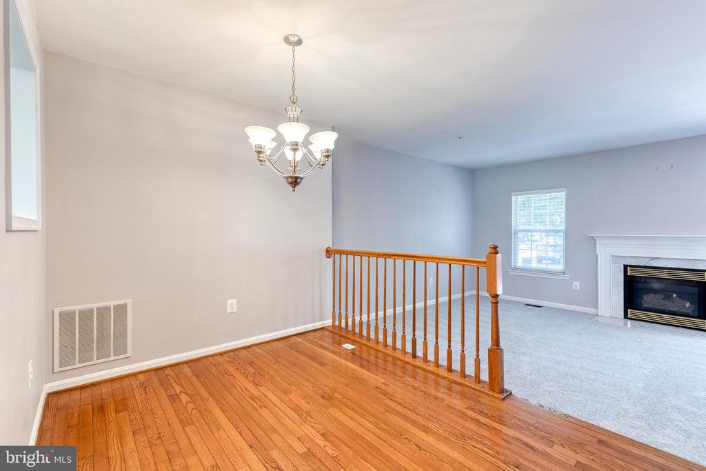 Hardwood-floored dining area beside a carpeted living room with a fireplace and wooden railing.
