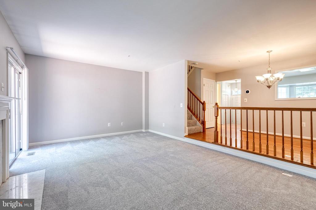 Carpeted living room with large windows overlooking a hardwood-floored area and staircase.