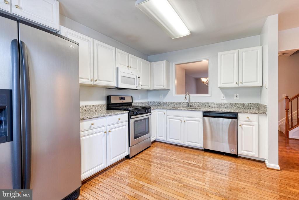 Kitchen with white cabinetry, granite countertops, stainless steel appliances, and hardwood floors.