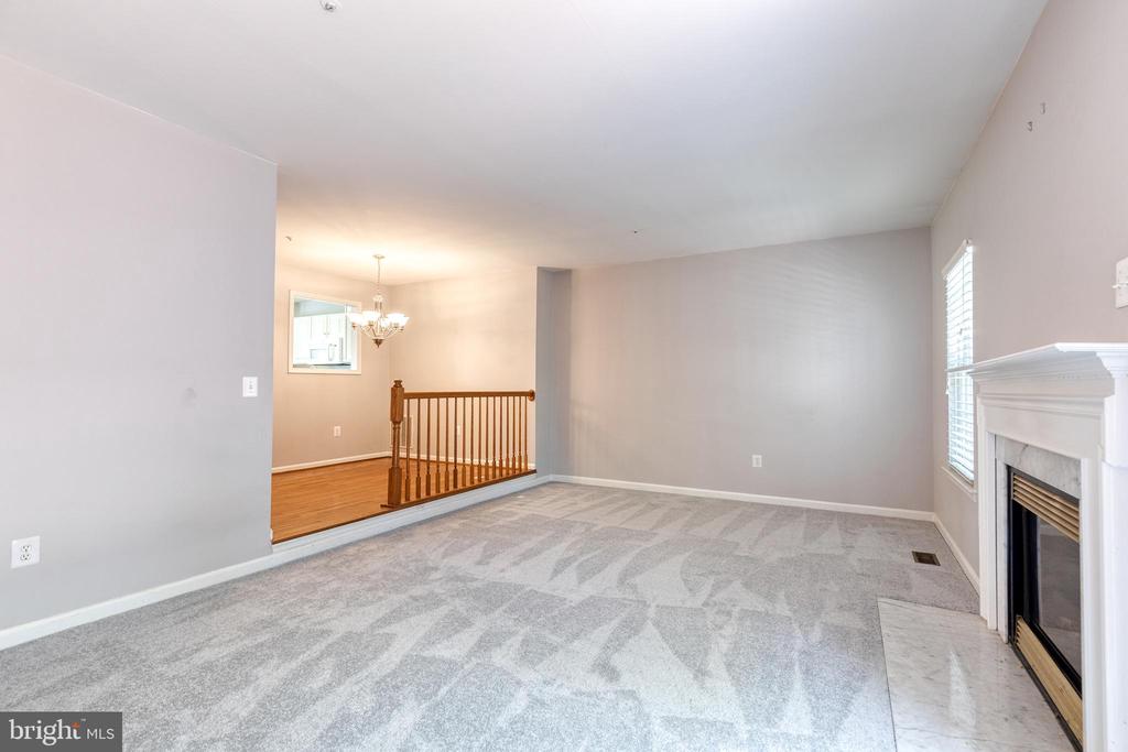 Unfurnished living room with patterned gray carpet, a white fireplace, and a view of the wood-floored landing.
