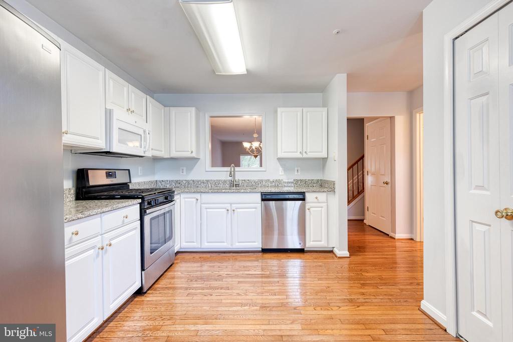 Kitchen with white cabinets, granite counters, stainless steel dishwasher, and hardwood floors extending into the hallway.