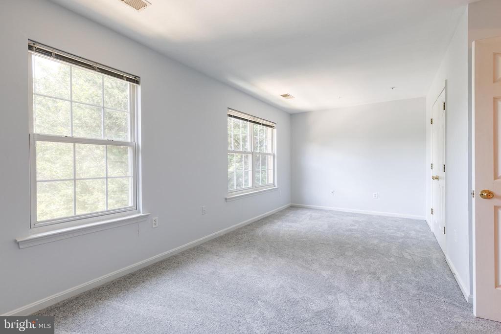 Vacant carpeted room with two large windows overlooking trees.