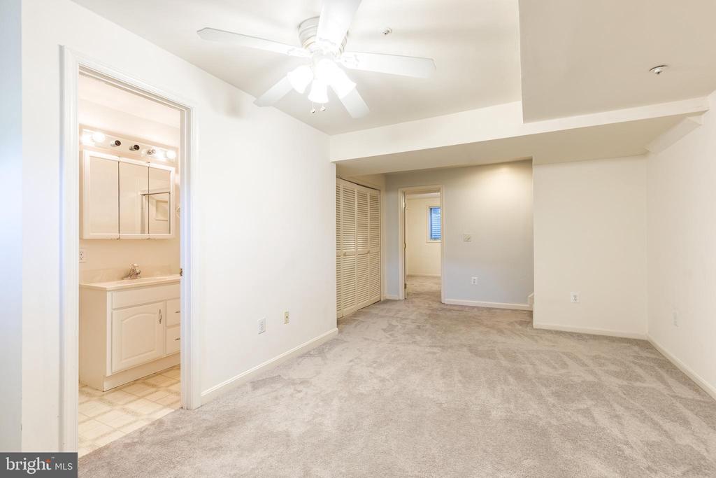 Vacant bedroom with a ceiling fan, louvered closet doors, and an adjoining bathroom vanity.