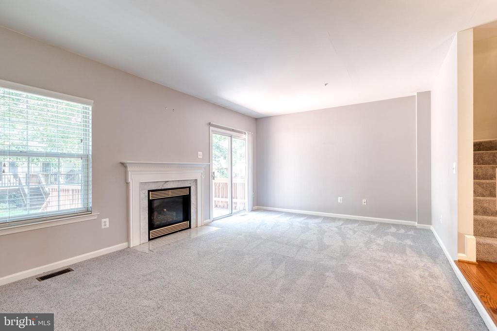 Empty living room with a fireplace, gray carpet, and large windows beside a sliding glass door.