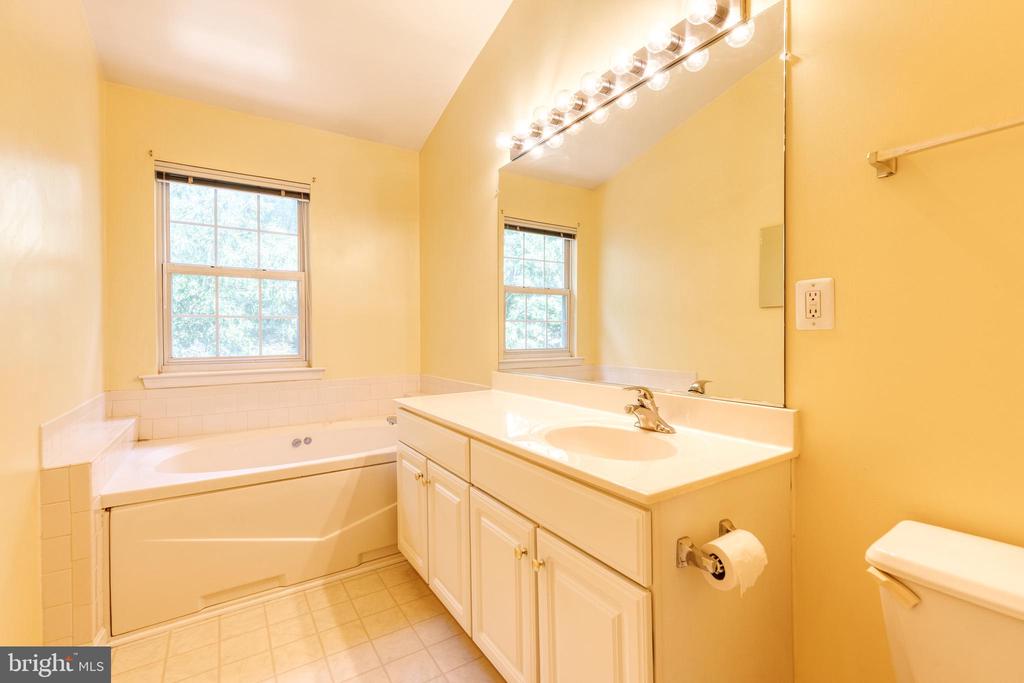 Bathroom with soaking tub, tiled surround, vanity, large mirror, and window.