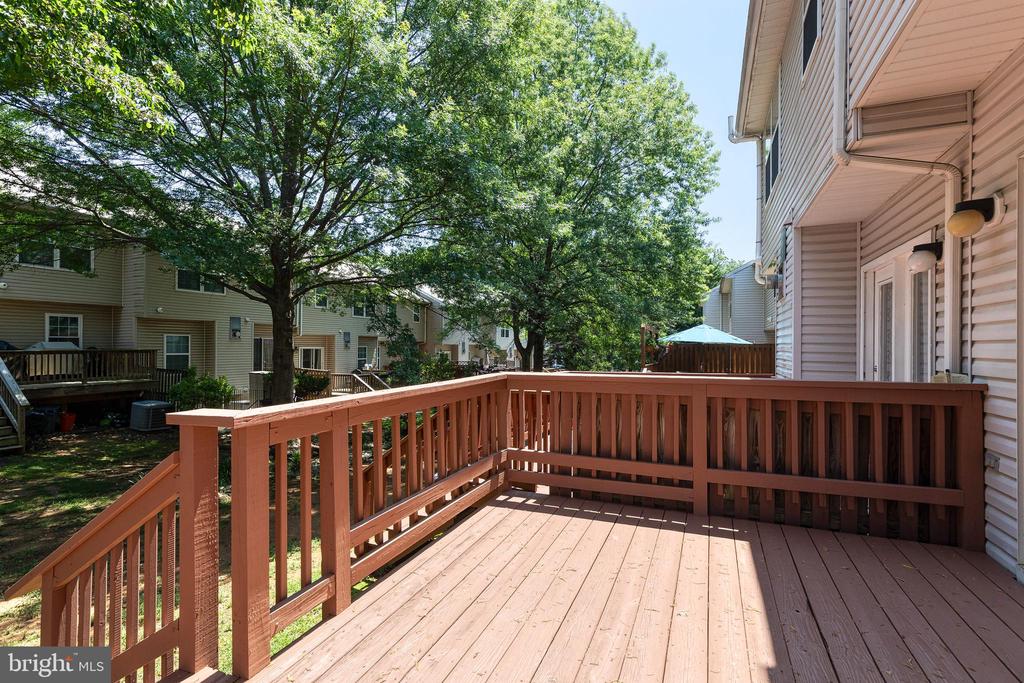 Wooden deck with reddish-brown railings overlooking leafy trees and neighboring homes.