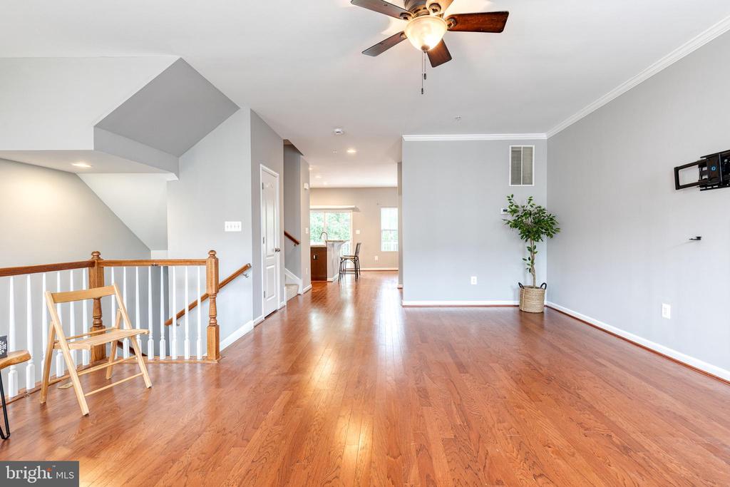 Open living area with reddish hardwood floors, a ceiling fan, and staircase railing.