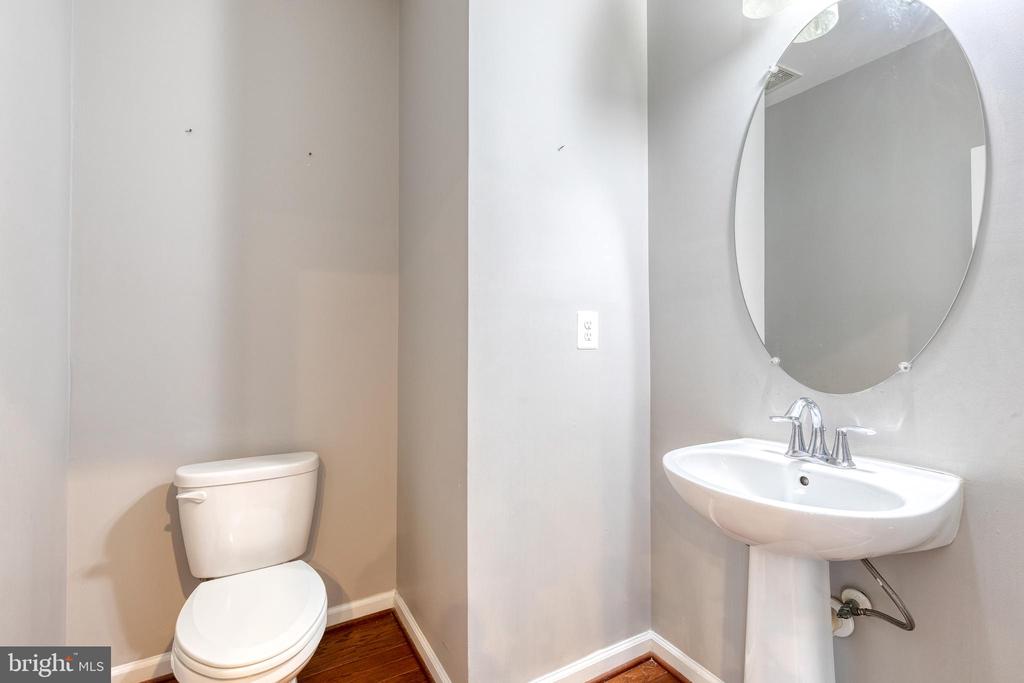 Bathroom with a toilet, pedestal sink, oval mirror, and reddish-brown wood floor.