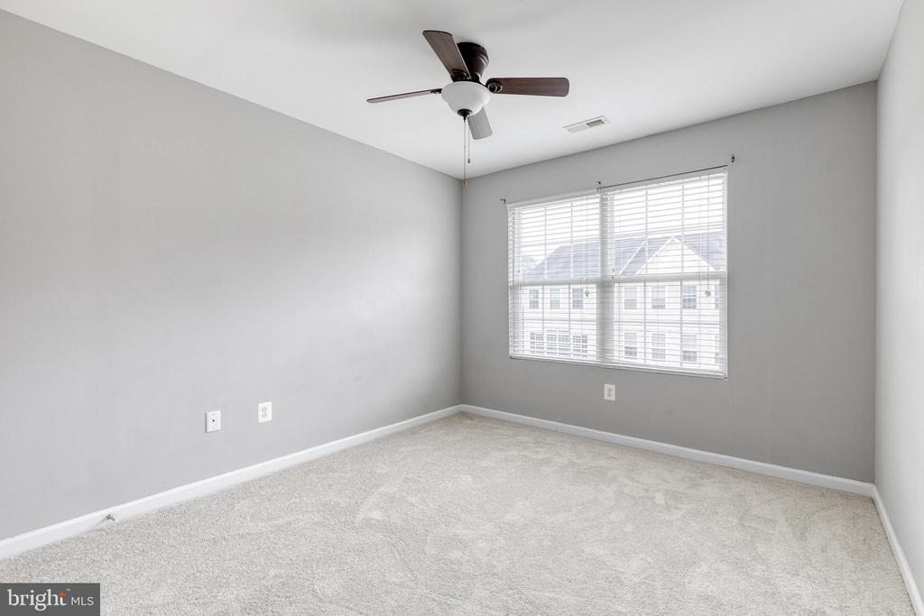 Empty bedroom with beige carpet, gray walls, a ceiling fan, and a large window with blinds.